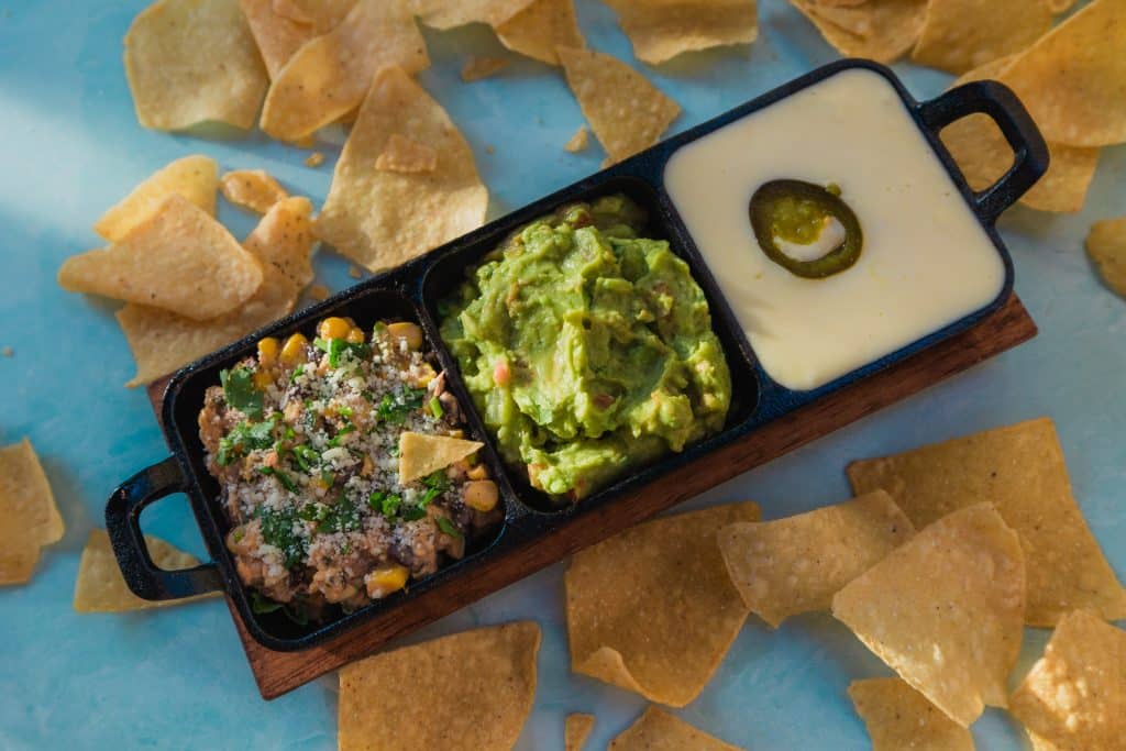 A serving dish with three different dips surrounded by tortilla chips.