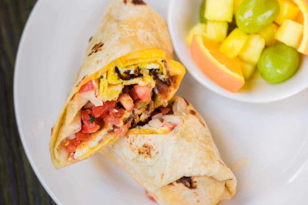 A wrap slice in half with a side of fruit.